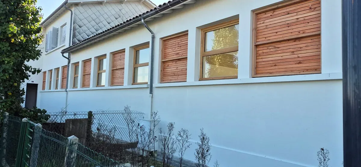 Façade habillée de bardage bois entre les fenêtres, avec descente d'eaux pluviales en zinc