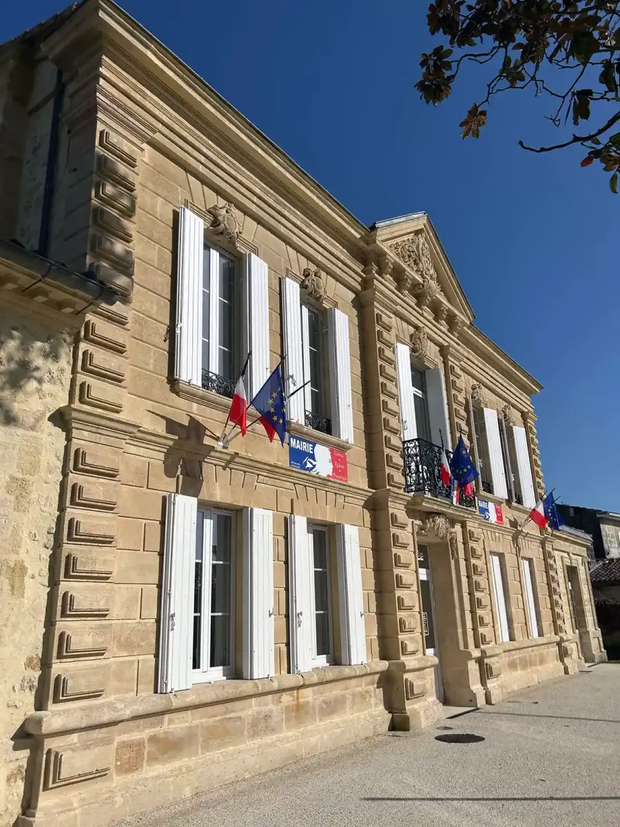 Façade d'une mairie en pierre de taille, pavoisée aux couleurs françaises et européennes