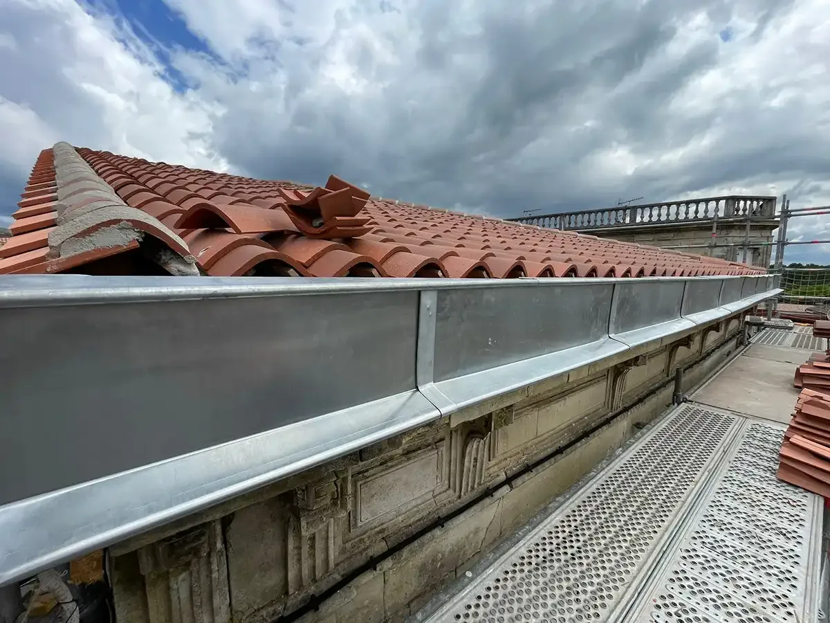 Chéneau en zinc neuf posé en pied de toiture, le long d'une balustrade en pierre